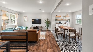 A modern living room with a sofa, TV, and dining area. - Midtown 4 BR for Work Stays and Home Transition (Little Rock)