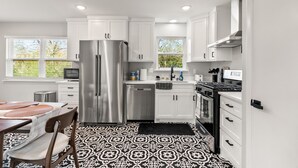 A modern kitchen with white cabinets, stainless steel appliances, and a patterned floor. - Midtown 4 BR for Work Stays and Home Transition (Little Rock)