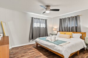 A bedroom with a wooden bed, grey curtains, a ceiling fan, and a bedside table with a lamp. - Midtown 4 BR for Work Stays and Home Transition (Little Rock)