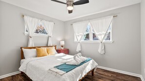 A bedroom with a bed, a nightstand, a ceiling fan, and two windows with curtains. - Midtown 4 BR for Work Stays and Home Transition (Little Rock)
