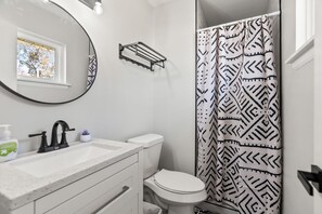 A bathroom with a white sink, black faucet, and a toilet. There is a shower curtain with a black and white geometric pattern. - Midtown 4 BR for Work Stays and Home Transition (Little Rock)