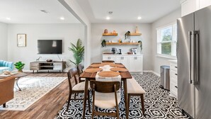 A modern kitchen with a dining area, white cabinets, a stainless steel refrigerator, and a flat-screen TV. - Midtown 4 BR for Work Stays and Home Transition (Little Rock)