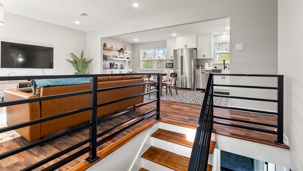 A modern living room with a brown sofa, a flat-screen TV, and a staircase with wooden steps. - Midtown 4 BR for Work Stays and Home Transition (Little Rock)