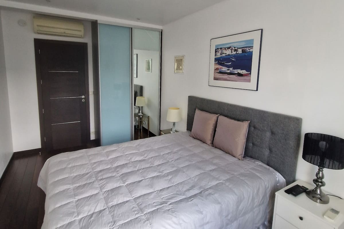 A bedroom with a large bed, a nightstand, a lamp, a framed picture on the wall, and a door.