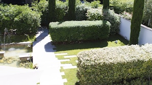 Um jardim bem cuidado, com um caminho pavimentado, sebes aparadas e diversas arbustos.