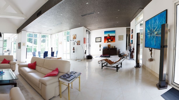 Uma sala de estar ampla, com um sofá vermelho, sofás bege e uma mesa de centro de vidro.