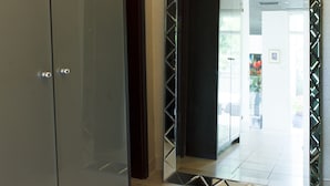 Corredor com um guarda-roupa grande e um espelho refletindo uma porta e um chão em azulejo.