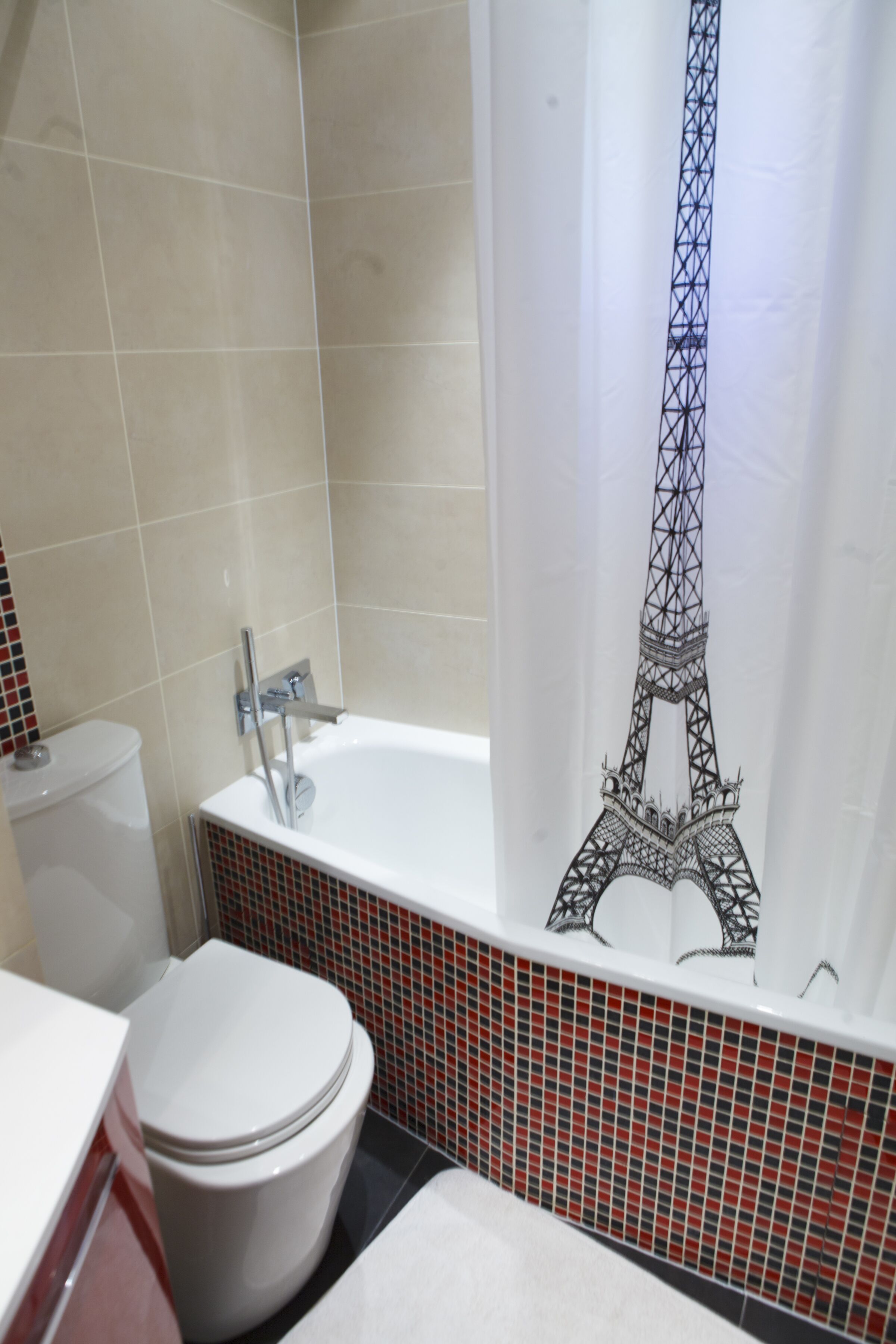 A bathroom with a white bathtub, a toilet, and a shower curtain depicting the Eiffel Tower.