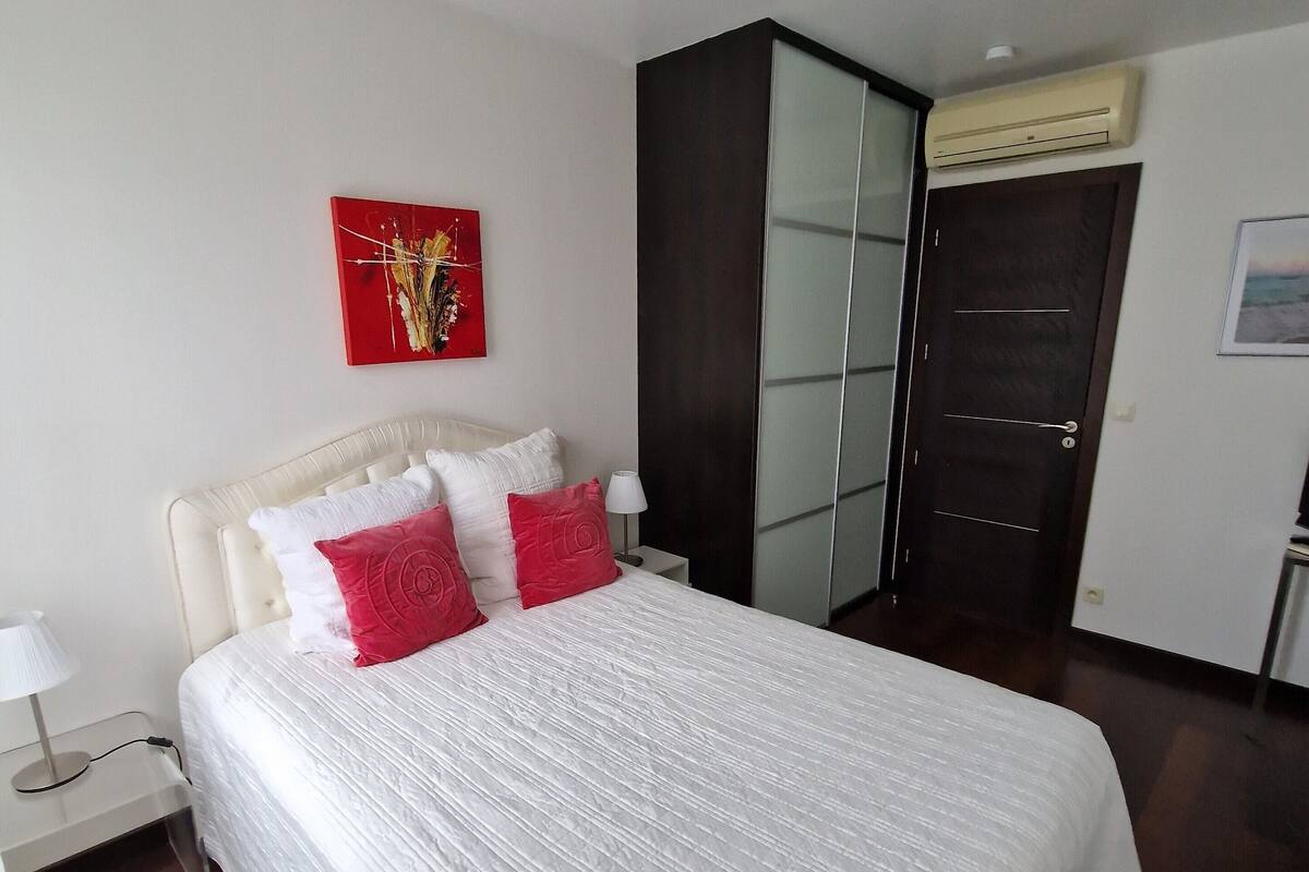 A hotel room with a large bed, a nightstand, a wardrobe, and a red artwork on the wall.