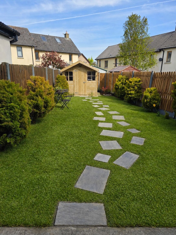 A well-maintained backyard with a stone pathway leading to a wooden shed, surrounded by a wooden fence and various shrubs.