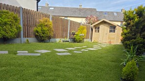 Un patio trasero bien cuidado con cerco de madera, un cobertizo y césped con piedras para pisar.