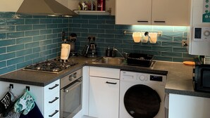 Cocina compacta con estufa a gas, horno, lavavajillas y lavadora. Incluye armarios, un lavabo y una lámpara en el techo.