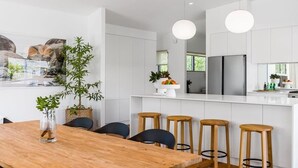 A modern kitchen with white cabinetry, a wooden dining table, and bar stools. - Ukiyo (Cabarita Beach)