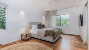 Een slaapkamer met een bed, nachtkastje, lamp en een aan de muur bevestigde televisie.