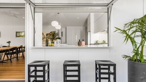 Una cuina moderna amb un finestral gran, una zona de dinar amb taula i cadires de fusta, i una planta en test.