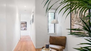 A hallway with a wooden floor, a brown leather sofa, a round table with books and a glass object, and a large plant. - Ukiyo (Cabarita Beach)