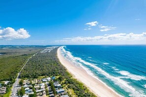 Luchtbeeld van een kustgebied met een strand, een weg en woongebouwen.