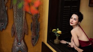 A room with a wooden fish decoration on the wall, a window with a view, and a vase with yellow flowers on the windowsill. - LA GAI HOMESTAY HOI AN (Da Nang)