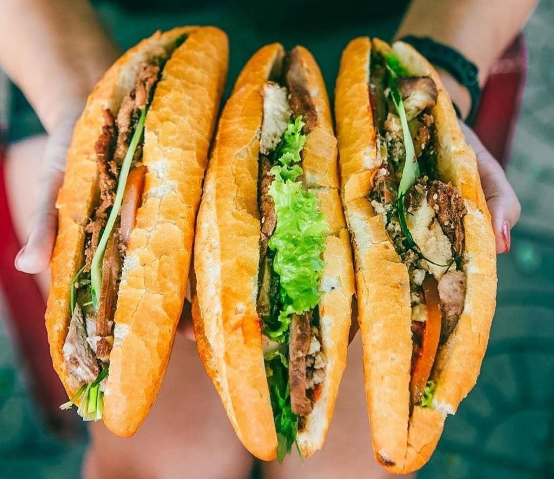 Una persona sosteniendo tres sándwiches.