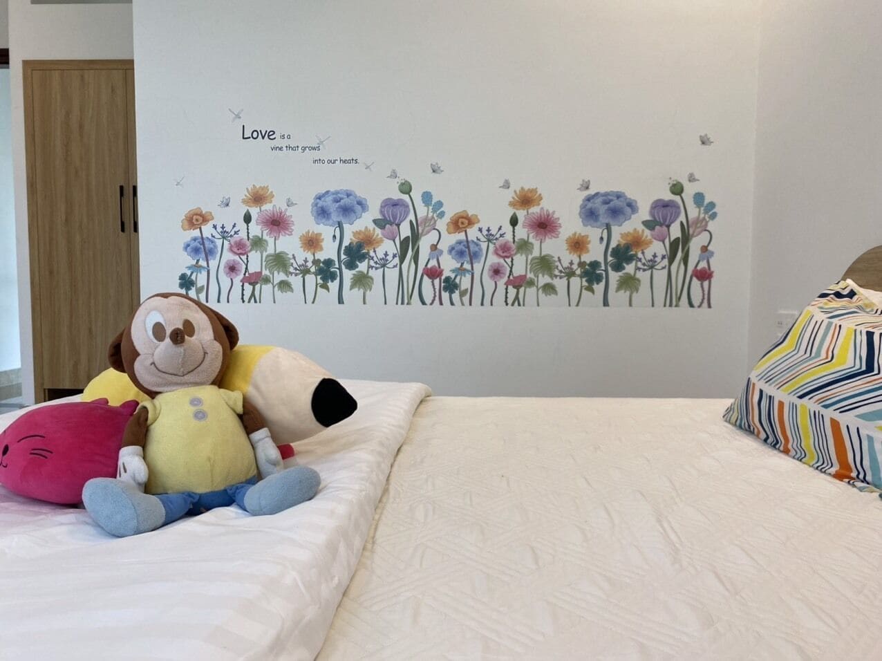 Une chambre avec un lit, un mur orné d’une fresque florale et un jouet en peluche représentant un singe.