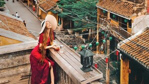 A woman sitting on a wooden ledge overlooking a traditional village with terracotta-roofed buildings and narrow streets. - LA GAI HOMESTAY HOI AN (Da Nang)