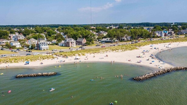 A coastal town with a sandy beach, a rocky breakwater, and residential buildings.