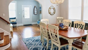 A dining area with a wooden table and white chairs, a chandelier, and a blue patterned rug.
