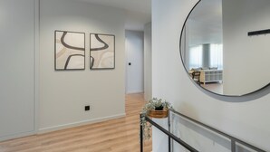 Un pasillo con suelo de madera, un espejo redondo y dos cuadros abstractos en la pared.