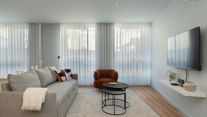 Una sala de estar moderna con un sofá gris, un sillón marrón, una mesita de centro redonda y un televisor montado en la pared.