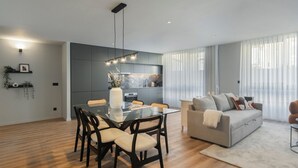 Una sala de estar moderna con un sofá gris, una mesa de comedor con sillas y una cocina con gabinetes grises y un salpicadero de mármol.
