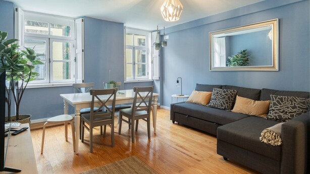 A modern living room with a grey sofa, a dining table with chairs, and a large mirror on the wall. - GuestReady - Calming retreat in Miragaia (Porto)
