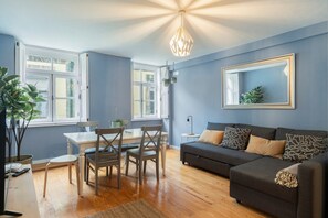 A modern living room with a grey sofa, a dining table with chairs, and a large mirror on the wall.
