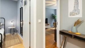 A hallway leading to a bedroom with a bed, bedside table, lamp, and a door. - GuestReady - Calming retreat in Miragaia (Porto)