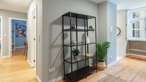 A modern interior with a black metal shelving unit against a grey wall, wooden flooring, and a large window. - GuestReady - Calming retreat in Miragaia (Porto)