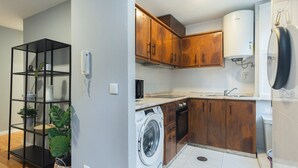 A compact kitchen with wooden cabinets, a washing machine, a microwave, and a water heater. - GuestReady - Calming retreat in Miragaia (Porto)