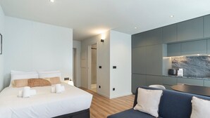 A modern bedroom with a large bed, a sofa, and a built-in kitchen area. - GuestReady - Trendy Studio Gaia (Vila Nova de Gaia)