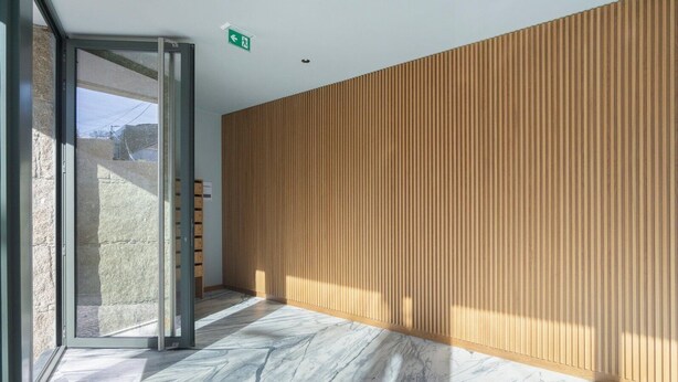A modern interior with a wooden panel wall, a glass door leading outside, and a marble floor. - GuestReady - Trendy Studio Gaia (Vila Nova de Gaia)