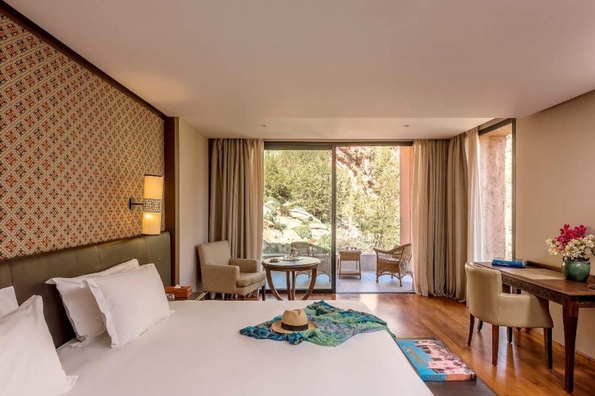A hotel room with a bed, a desk, a chair, and a view of the outdoors.