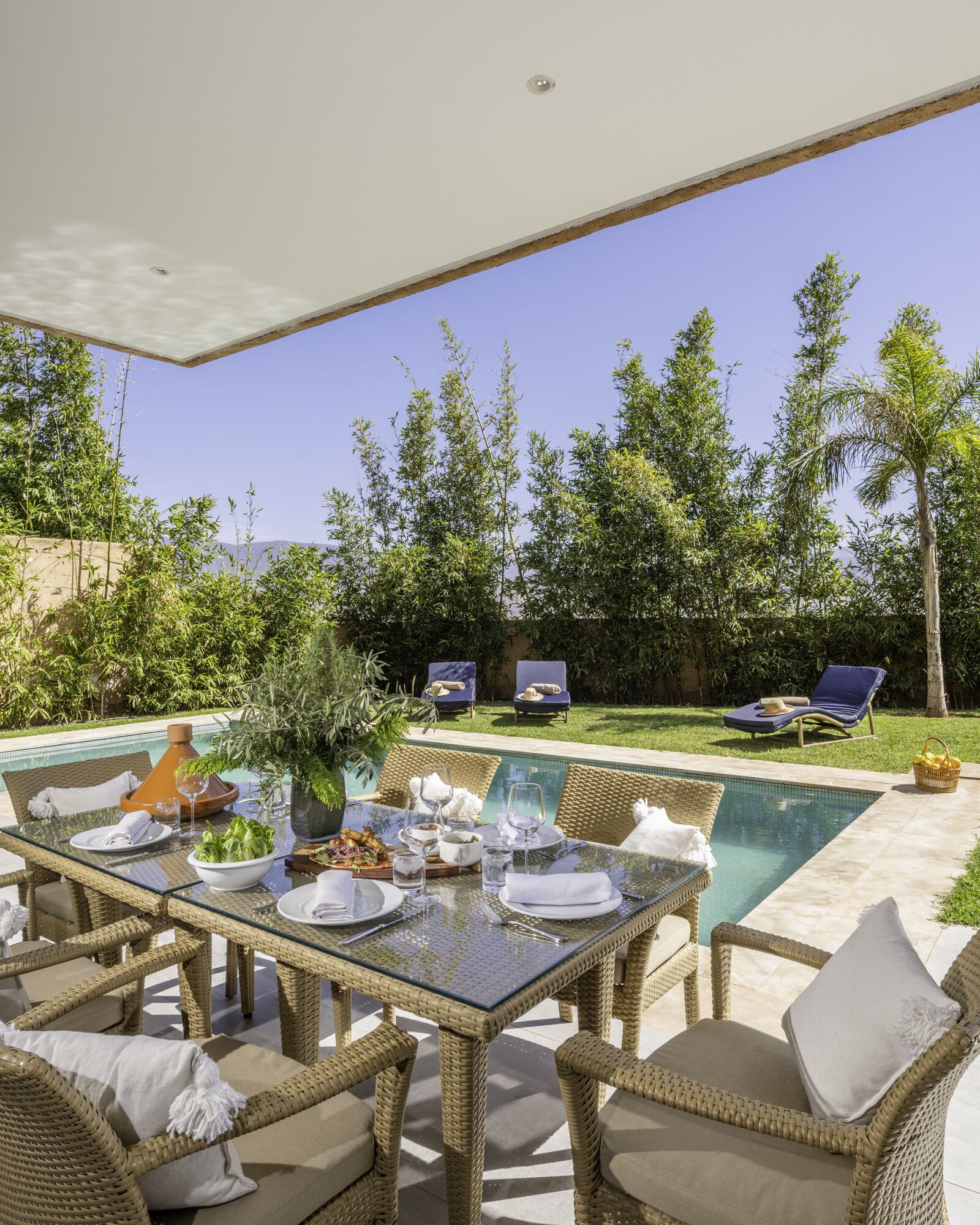 Un área de comedor al aire libre con mobiliario de mimbre y una piscina.