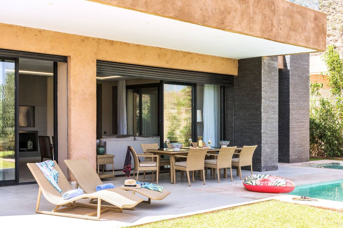 Un espacio exterior moderno con piscina, sillas de descanso y mesa de comedor.