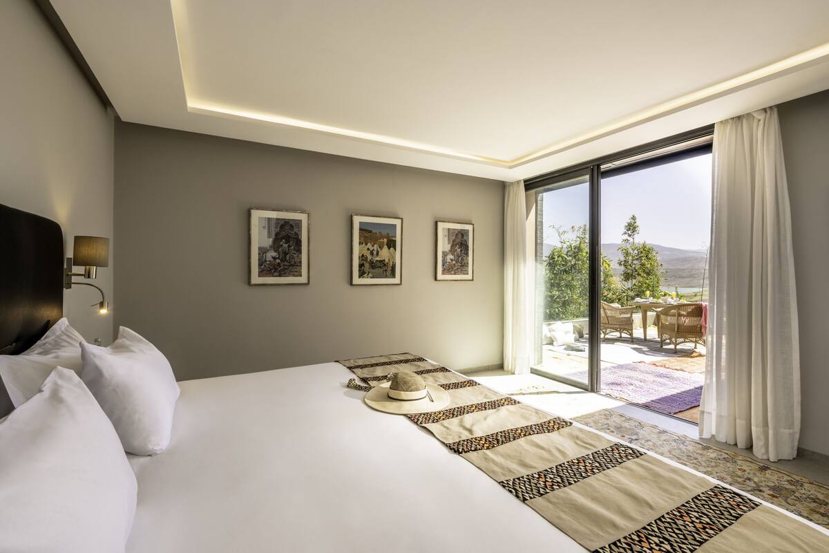 Habitación de hotel con una cama grande, vistas al exterior y un balcón con mobiliario.