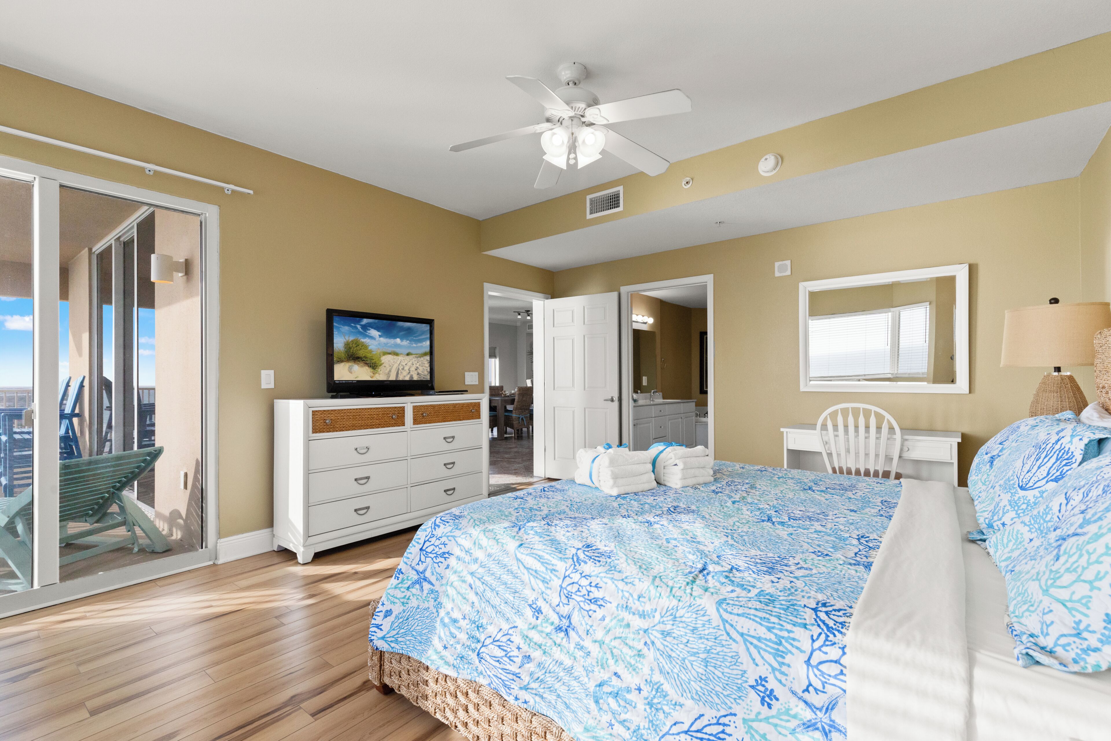 A bedroom with a large bed, a ceiling fan, a television, a sliding glass door, and a view of the outdoors.