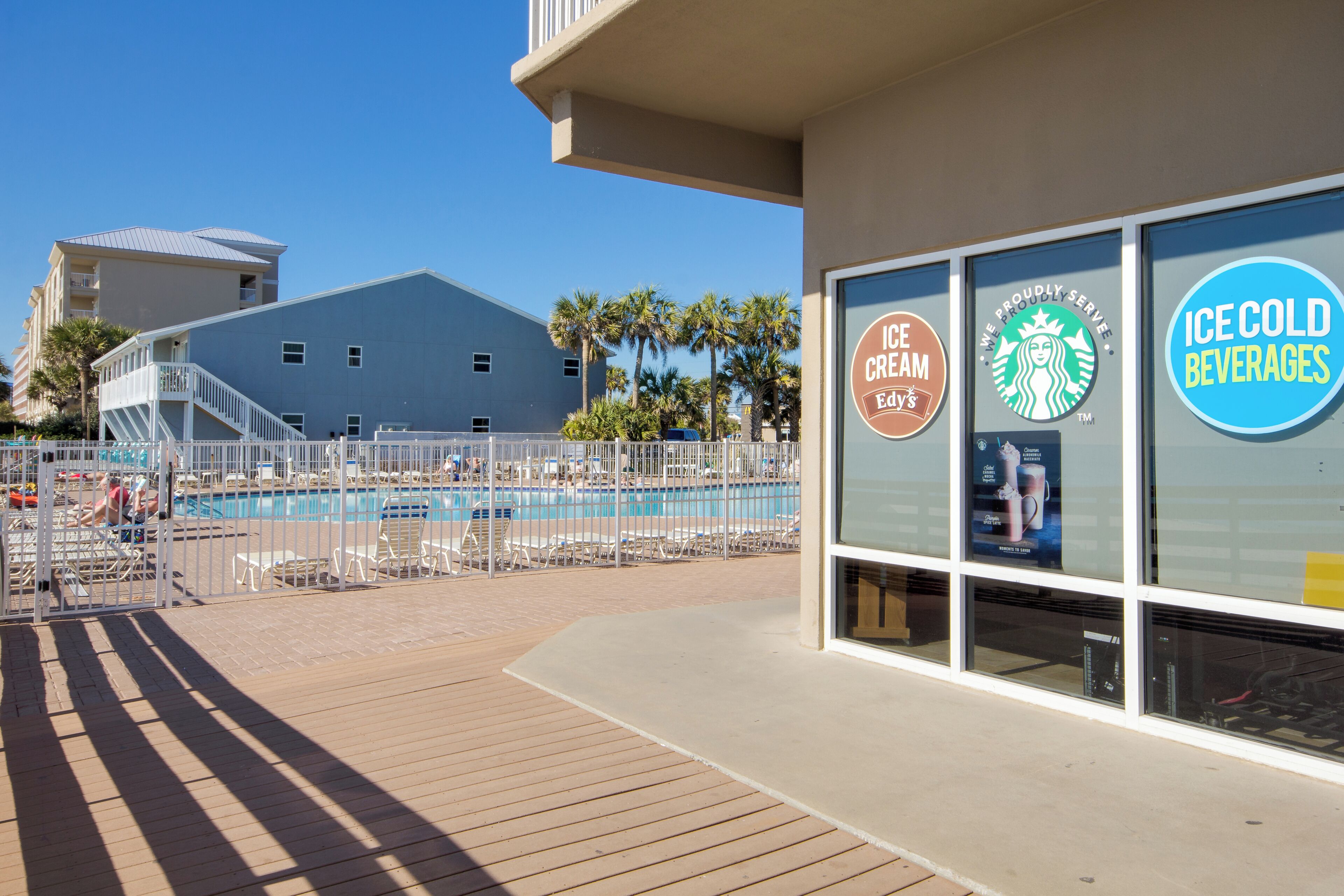 Zona de piscina con un edificio que muestra el logo de Starbucks y un letrero que indica 'Bebidas bien frías'.
