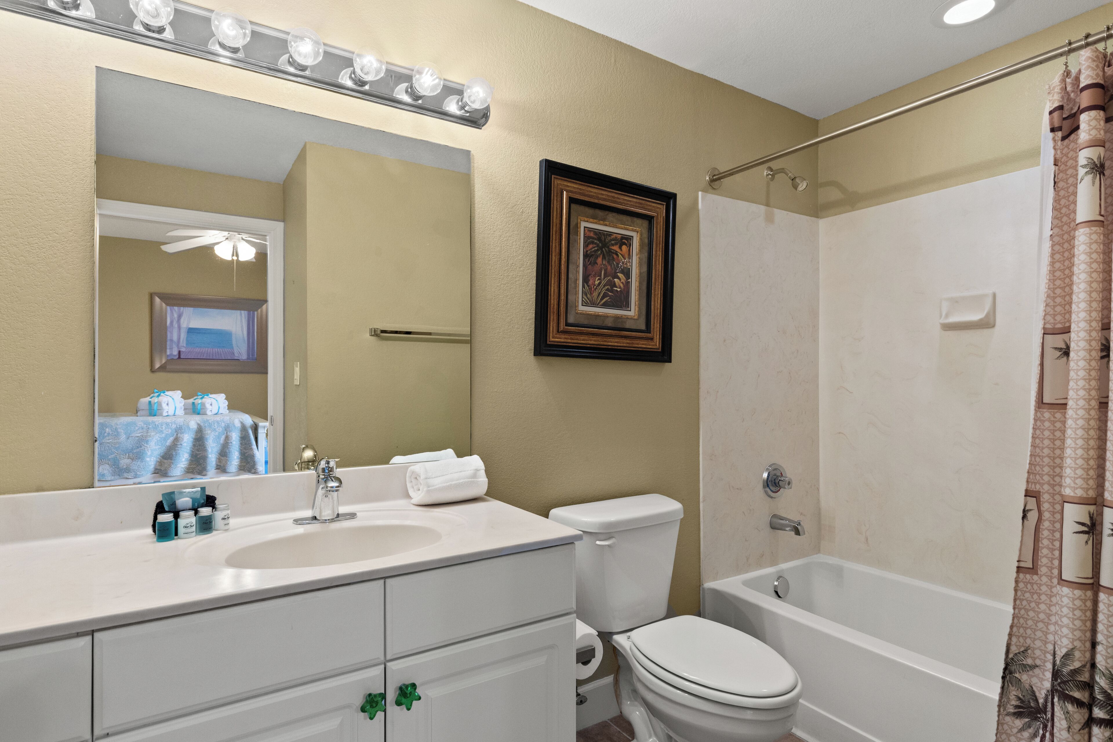 Ein Badezimmer mit Waschbecken, Toilette und Badewanne, einem Spiegel mit Beleuchtung und einem gerahmten Bild an der Wand.