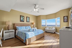 Un dormitorio con cama, mesitas de noche, escritorio, ventilador de techo y ventana con persianas.
