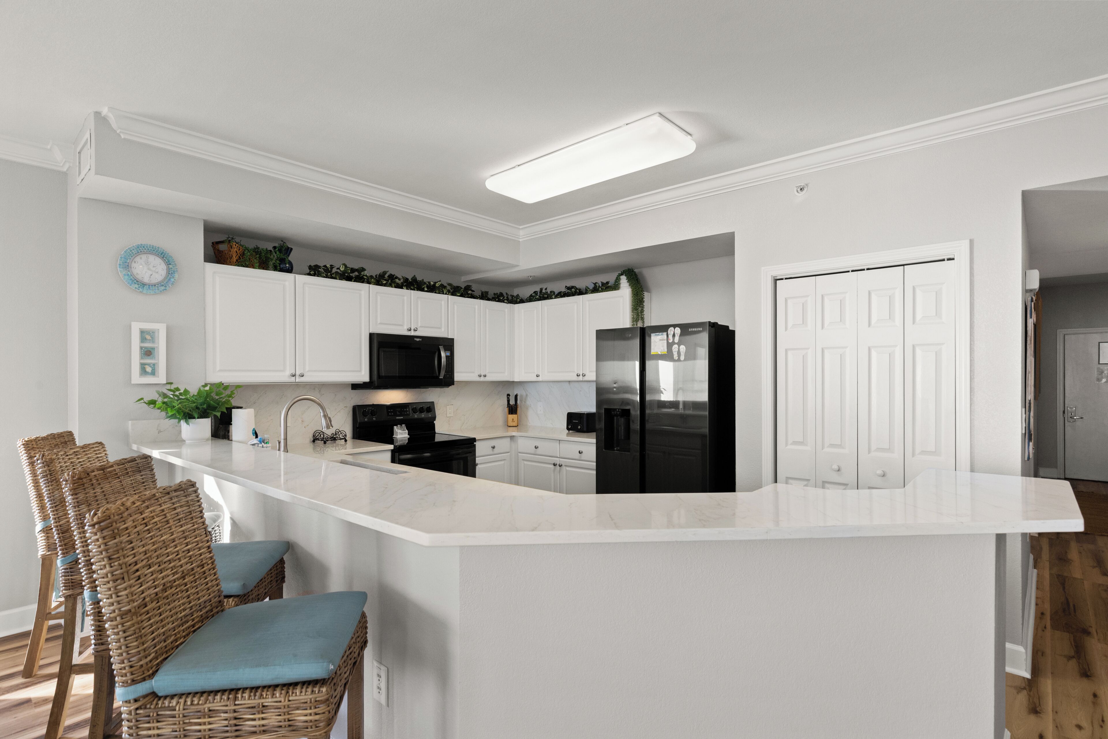 A modern kitchen with white cabinetry, a central island, bar stools, and a refrigerator.