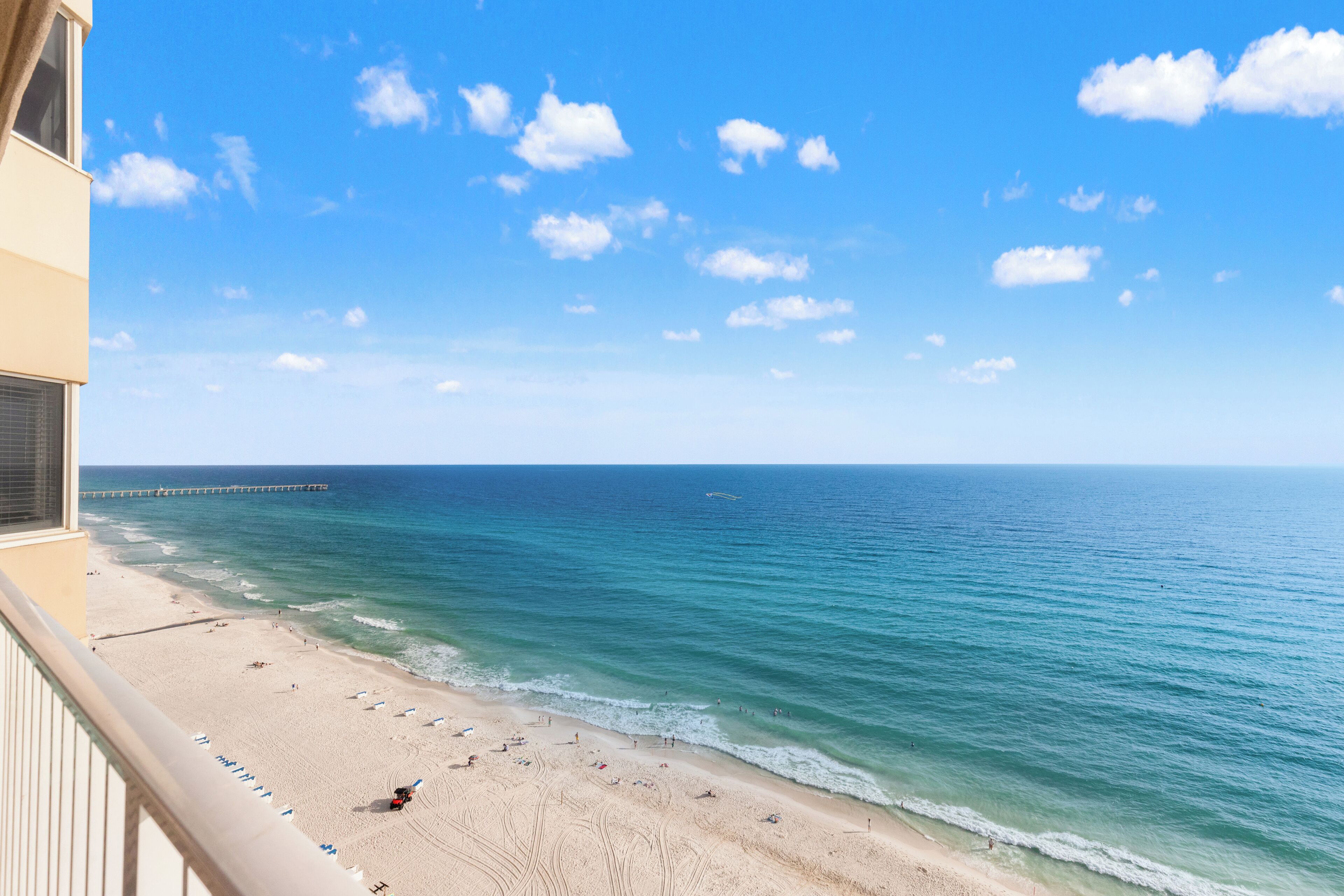 Une vue sur la plage avec une jetée qui s’avance dans l’océan, une plage de sable avec des parasols et un ciel dégagé.