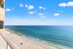 A beach view with a pier extending into the ocean, a sandy beach with umbrellas, and a clear sky.