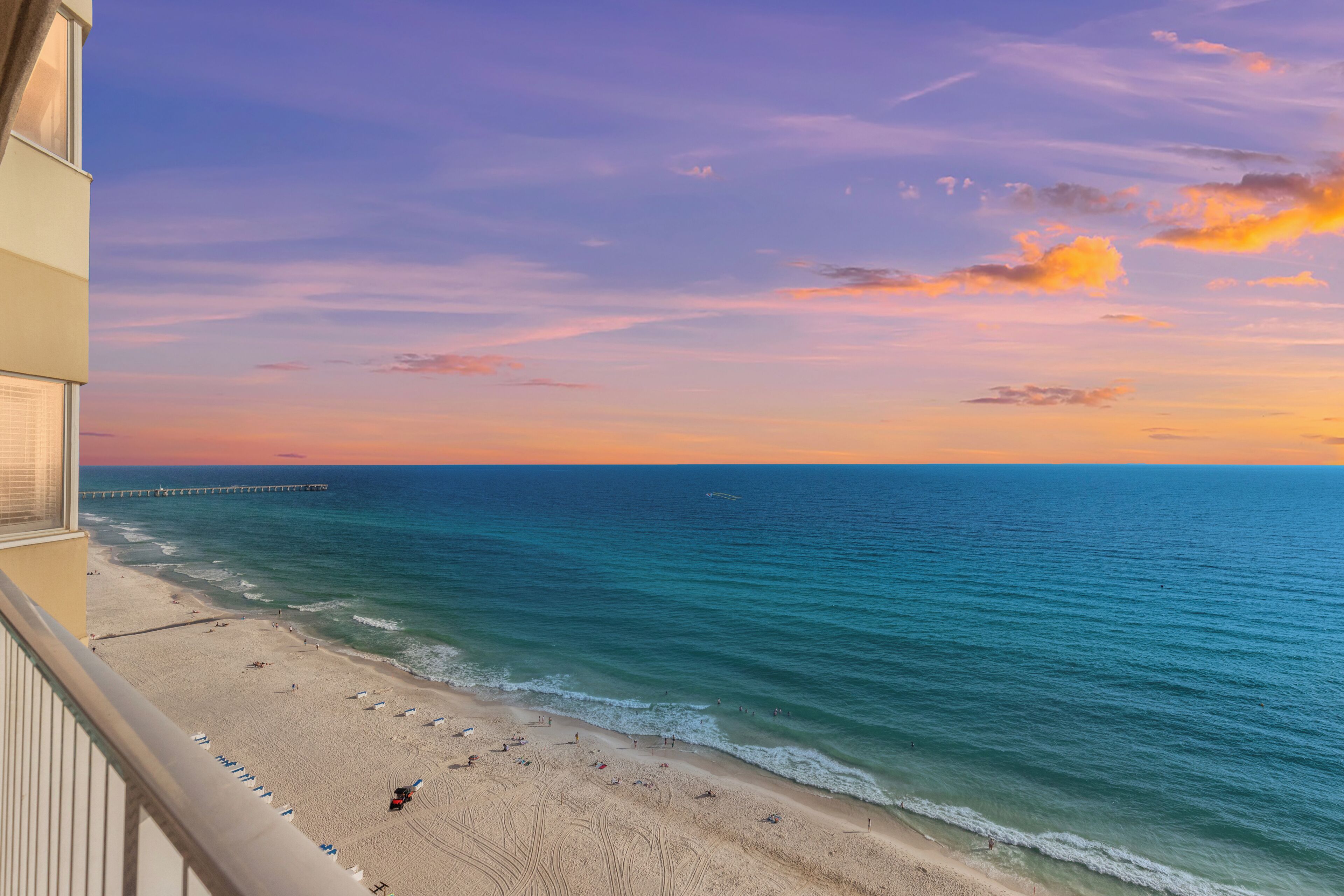 Blick auf einen Strand mit einem Steg, der sich ins Wasser erstreckt, feinem Sand und einem klaren Himmel.