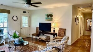 A living room with wicker furniture, a television, and a clock on the wall.